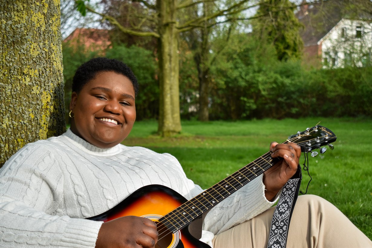 Eine Frau mit Gitarre lehnt an einem Baum